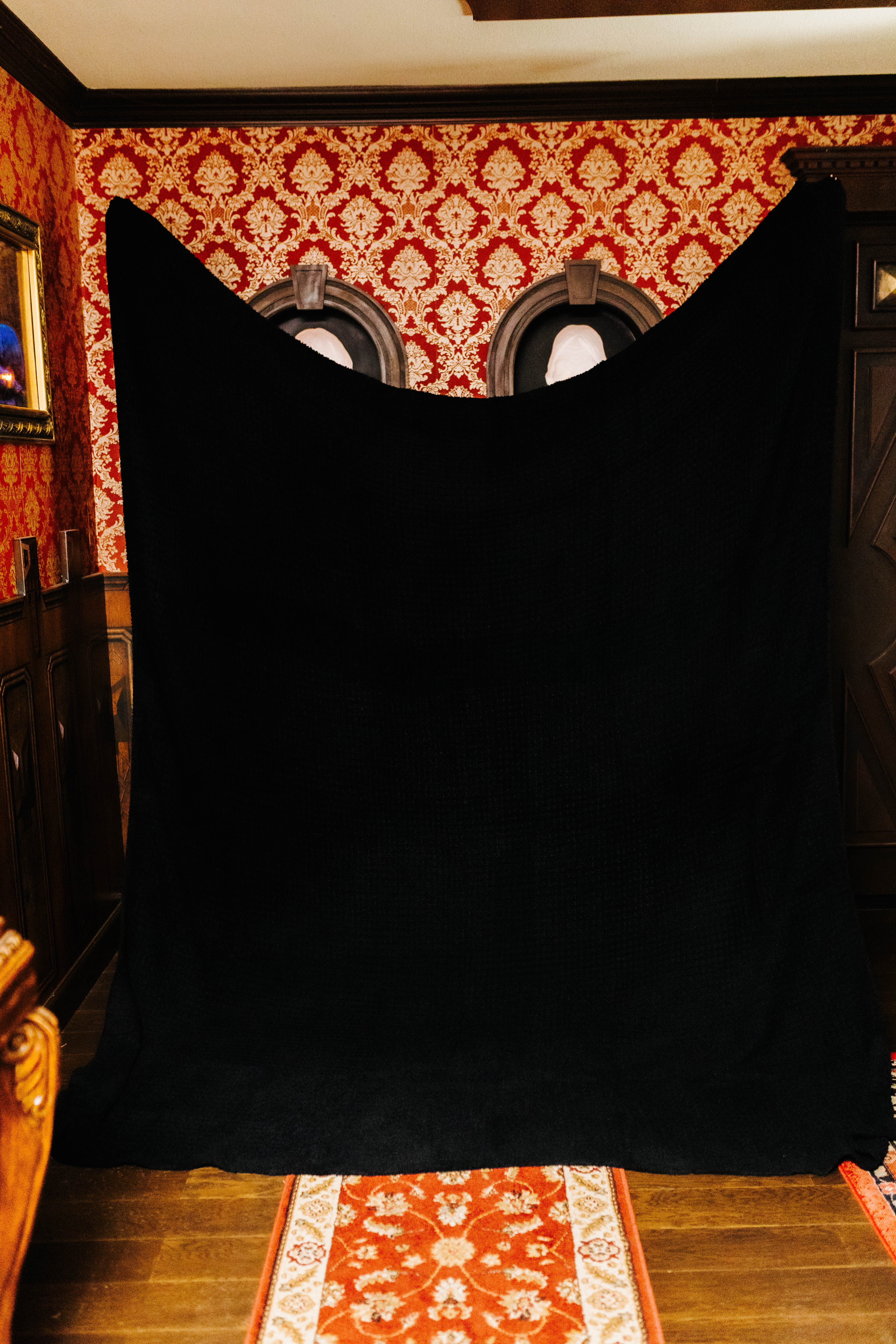 holding up the black non fringe blanket against a patterned wall