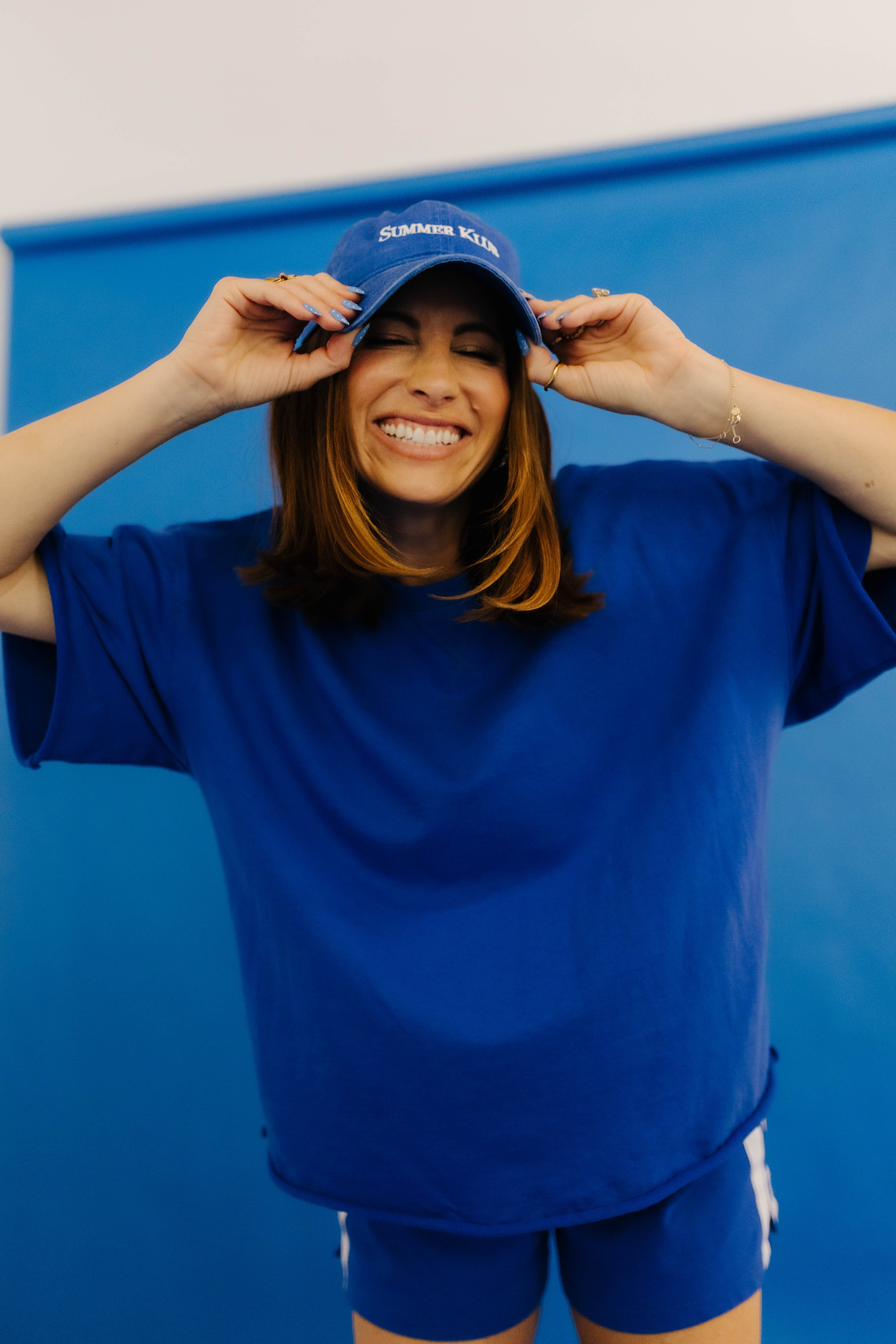 Person wearing a blue shirt and shorts with a blue cap, standing against a blue background