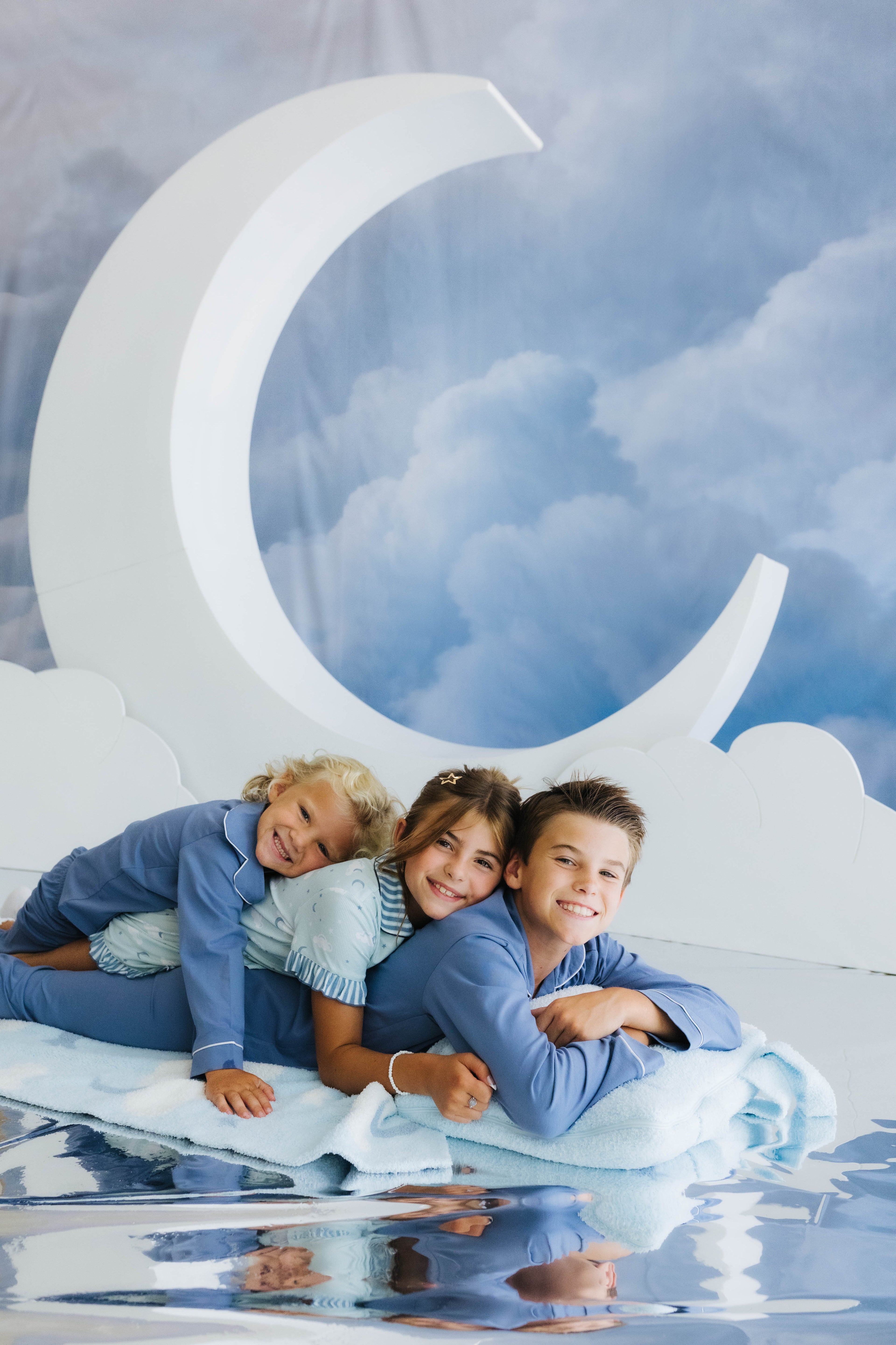 kids piled on top of one another smiling with cloud backpack/wristlet quillow and cloud and moon decorations in the back 