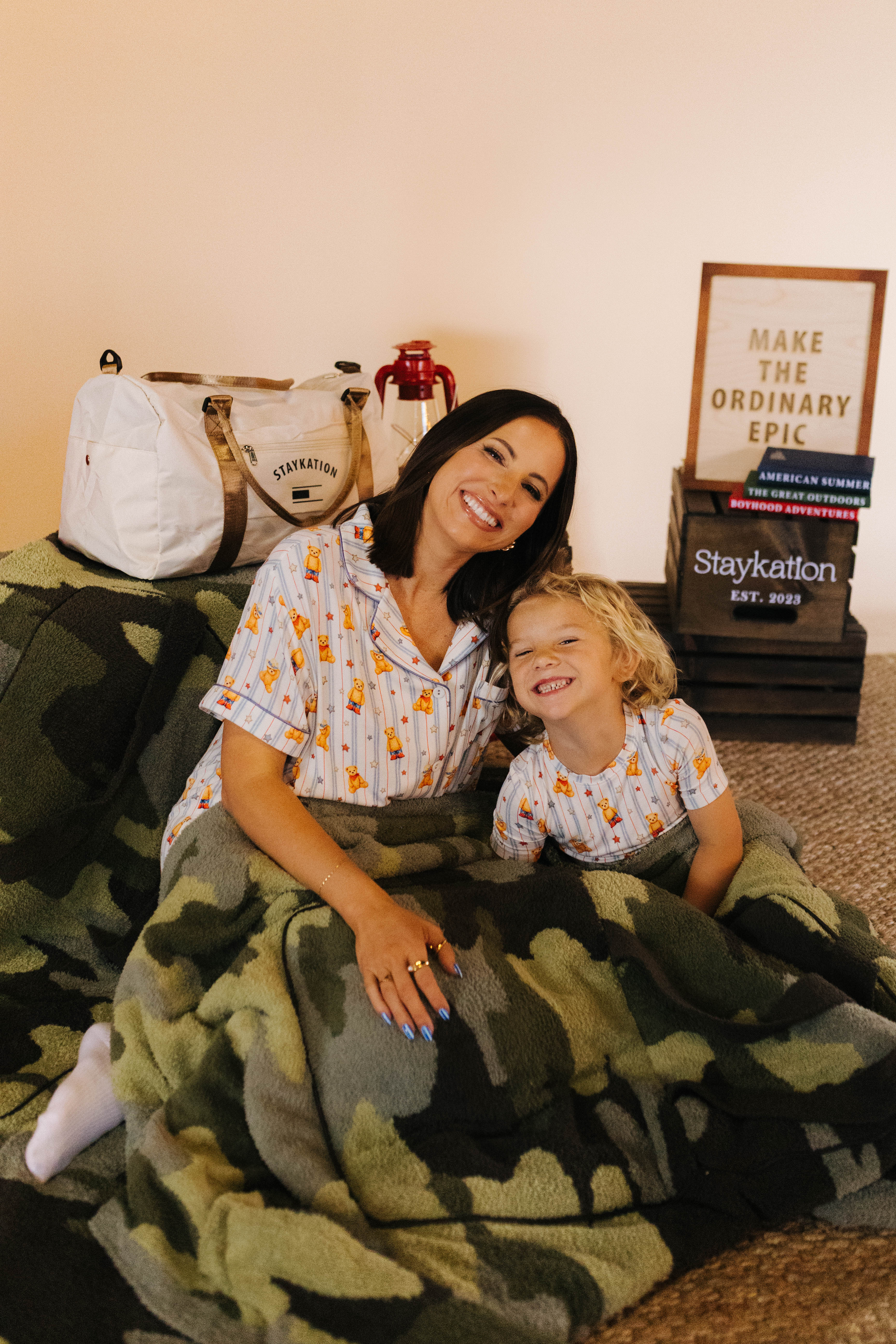 Kamp and Krista sitting on a rug with the camo quillow over them and decor behind them