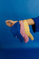 Three colorful caps (blue, pink, yellow) held by a hand against a blue background