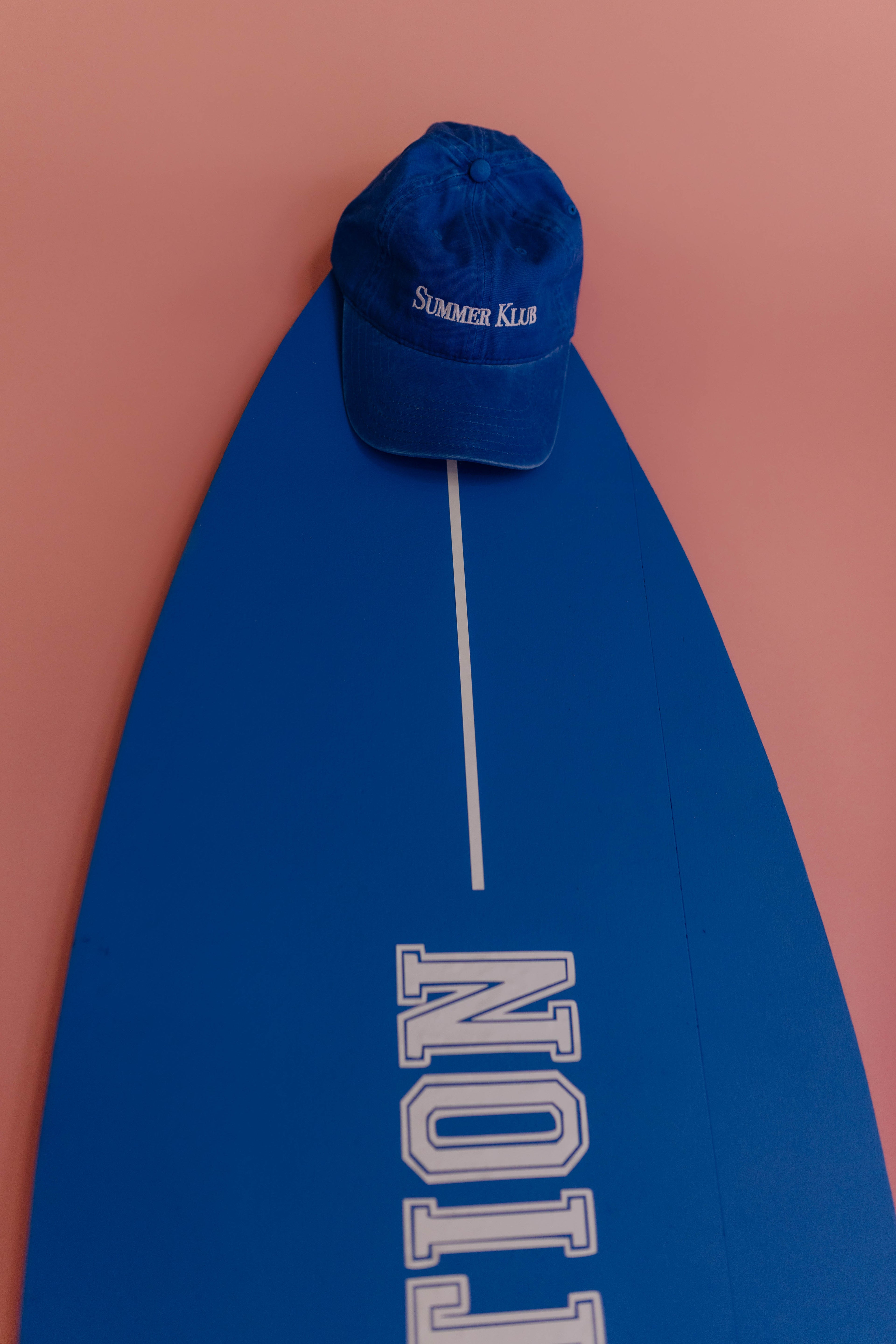 Blue cap on a blue surfboard with 'Summer King' text against a pink background