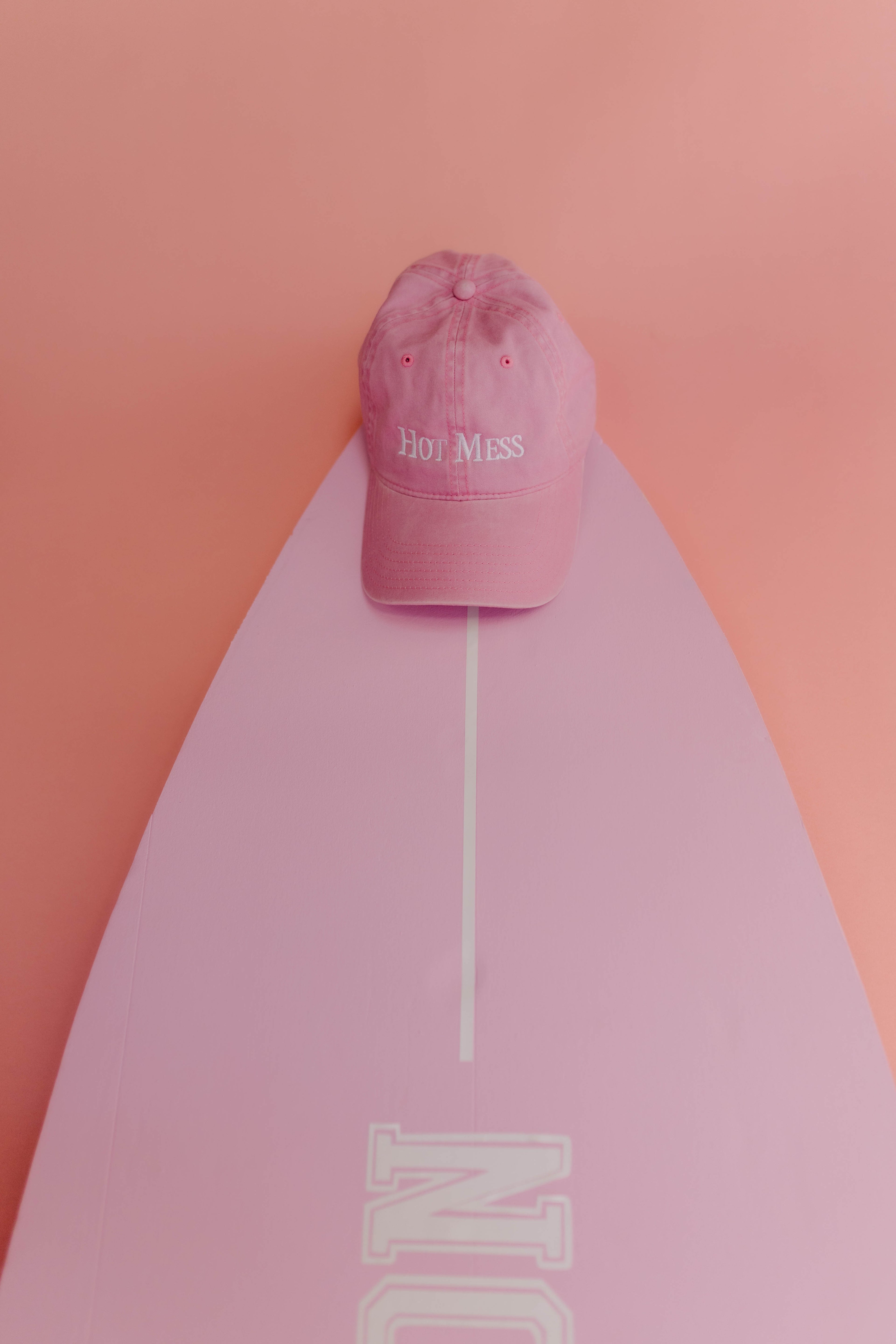 Pink cap with 'Hot Mess' text on a pink surfboard against a pink background