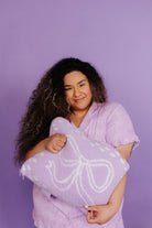 Woman holding a purple quillow with a white bow design against a purple background