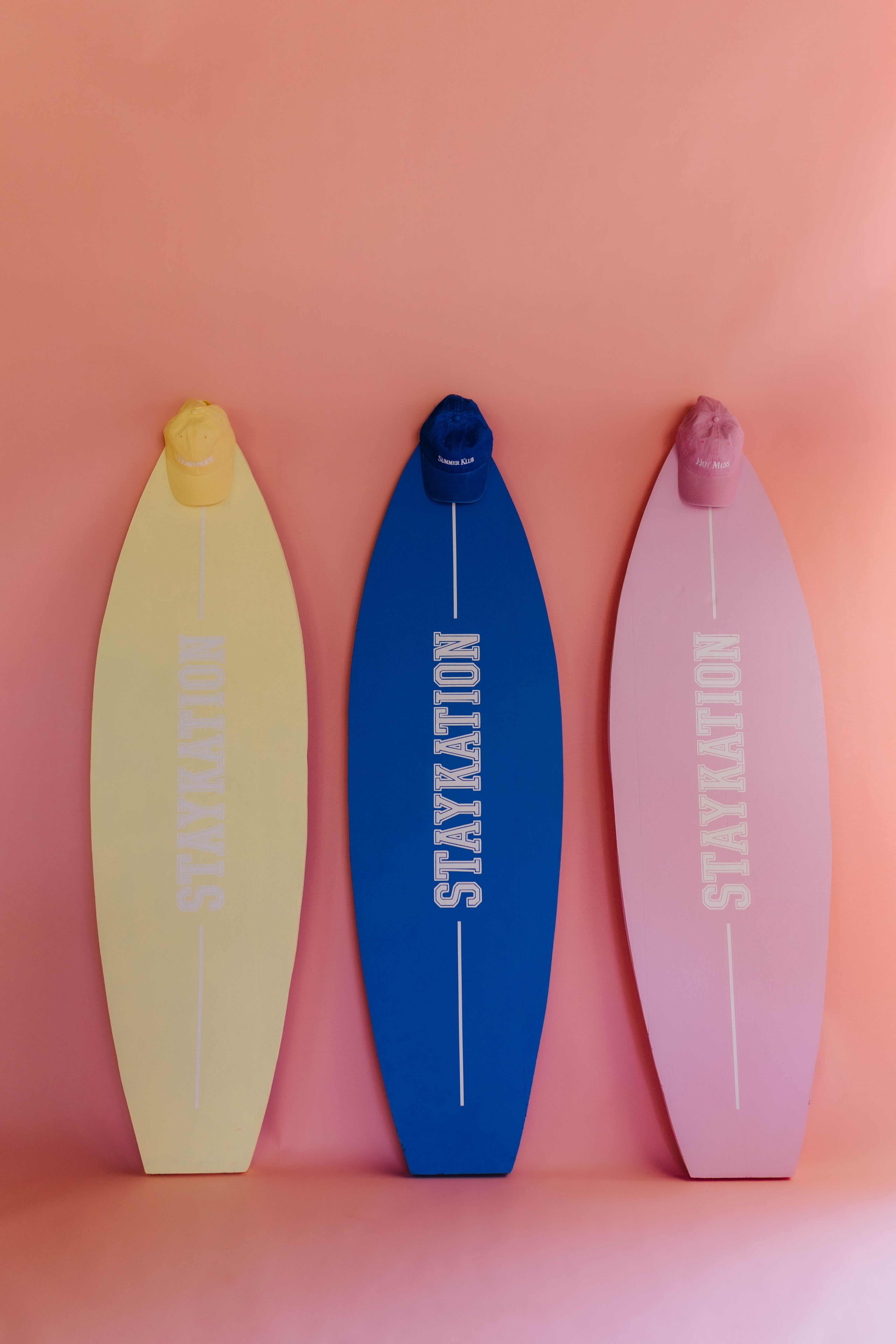 Three surfboards with 'STAYKATION' branding on a pink background