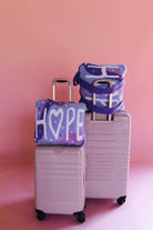 Two pastel pink hard-shell suitcases with matching quillows that say hope
