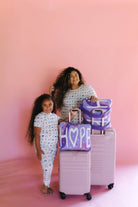 A woman and a young girl wearing matching pjs holding matching suitcases with the matching quillows that say hope