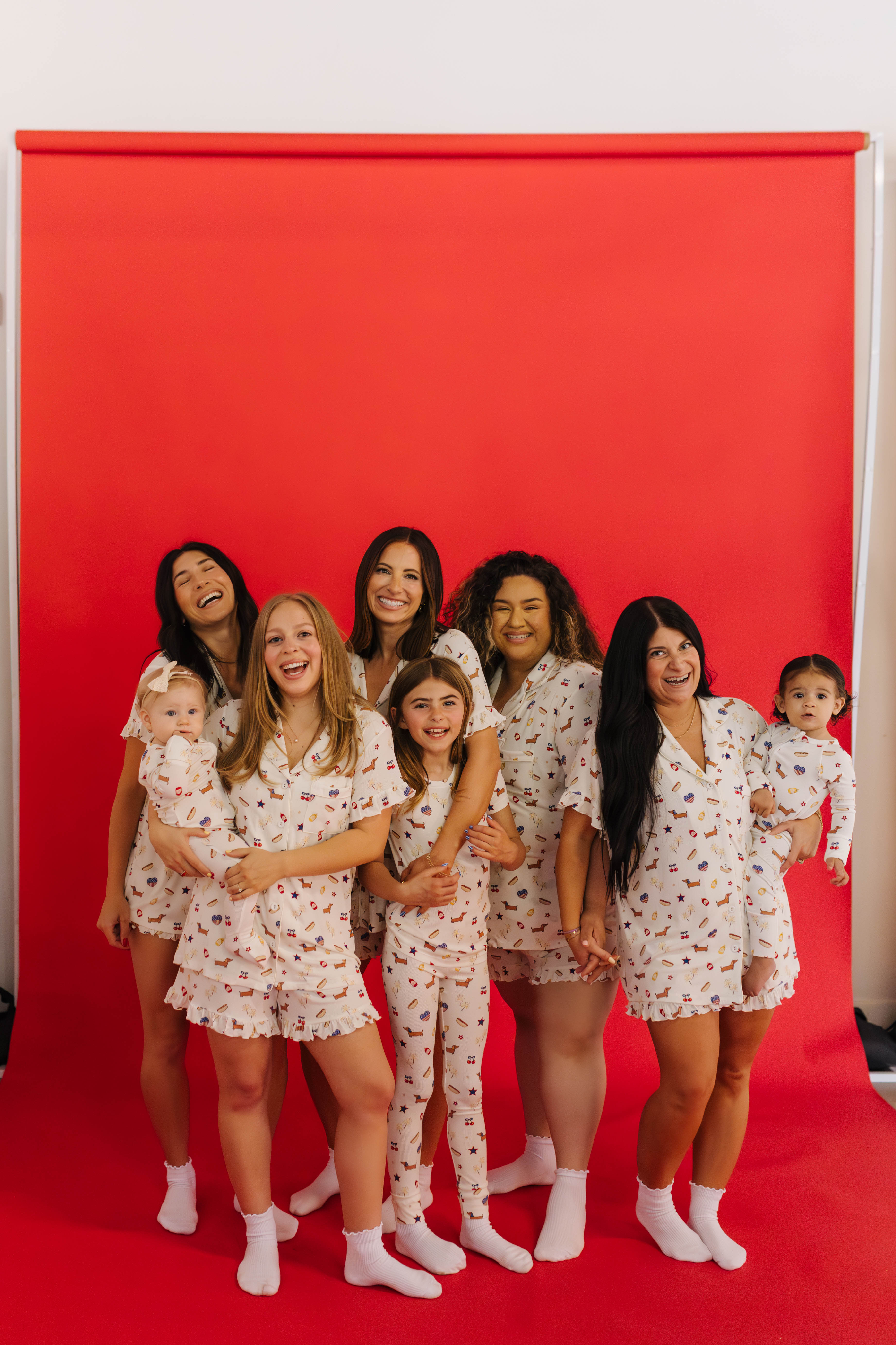 Group of women and children in matching pajamas standing against a red backdrop