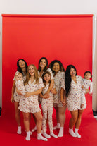 Group of women and children in matching pajamas standing against a red backdrop