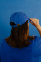Person wearing a blue cap against a blue background showing back of hat