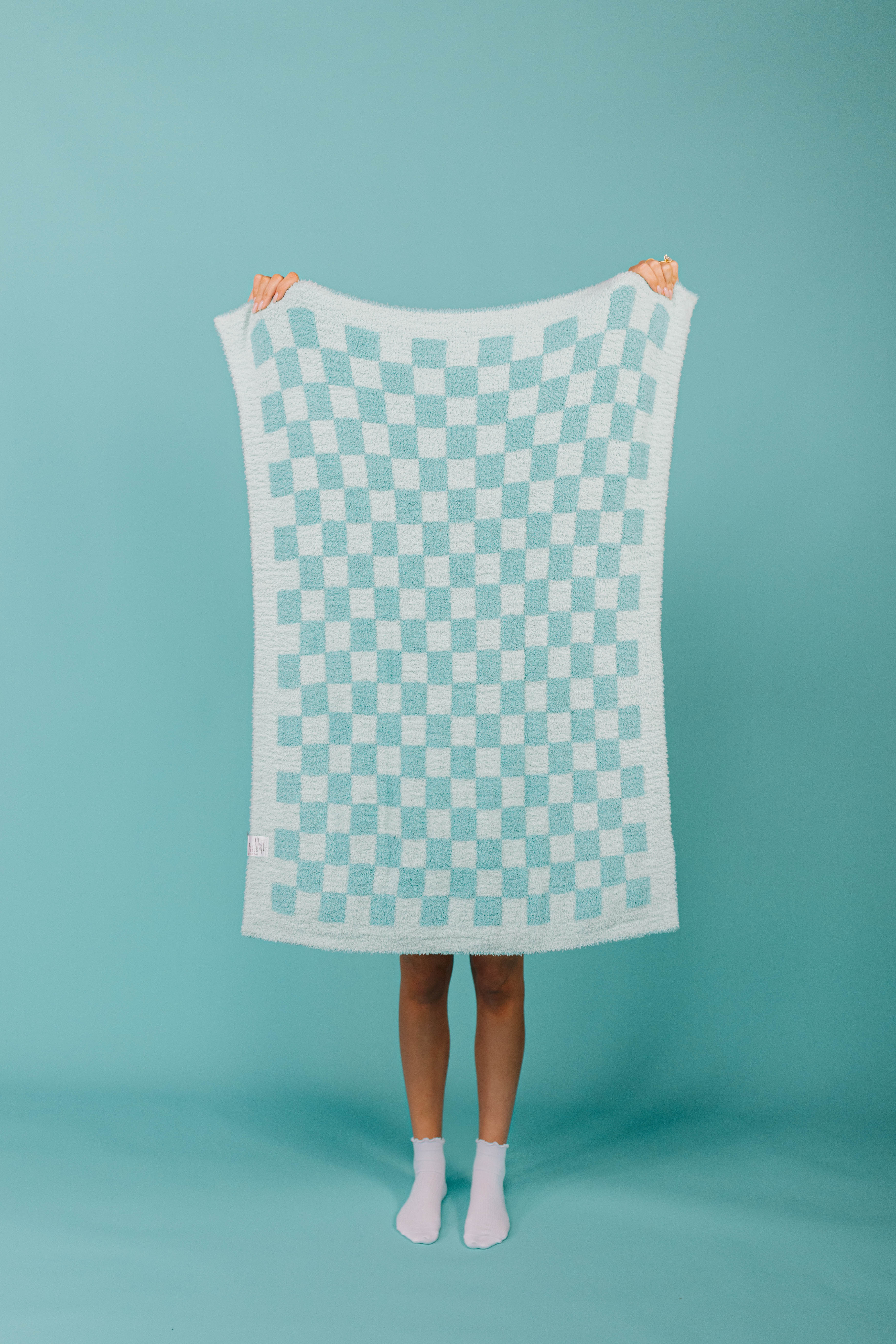 Person holding a checkered blanket against a teal background
