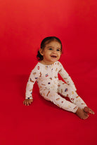 Child wearing a white onesie with colorful patterns on a red background