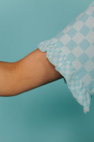 Checkered fabric with ruffled edge on a teal background