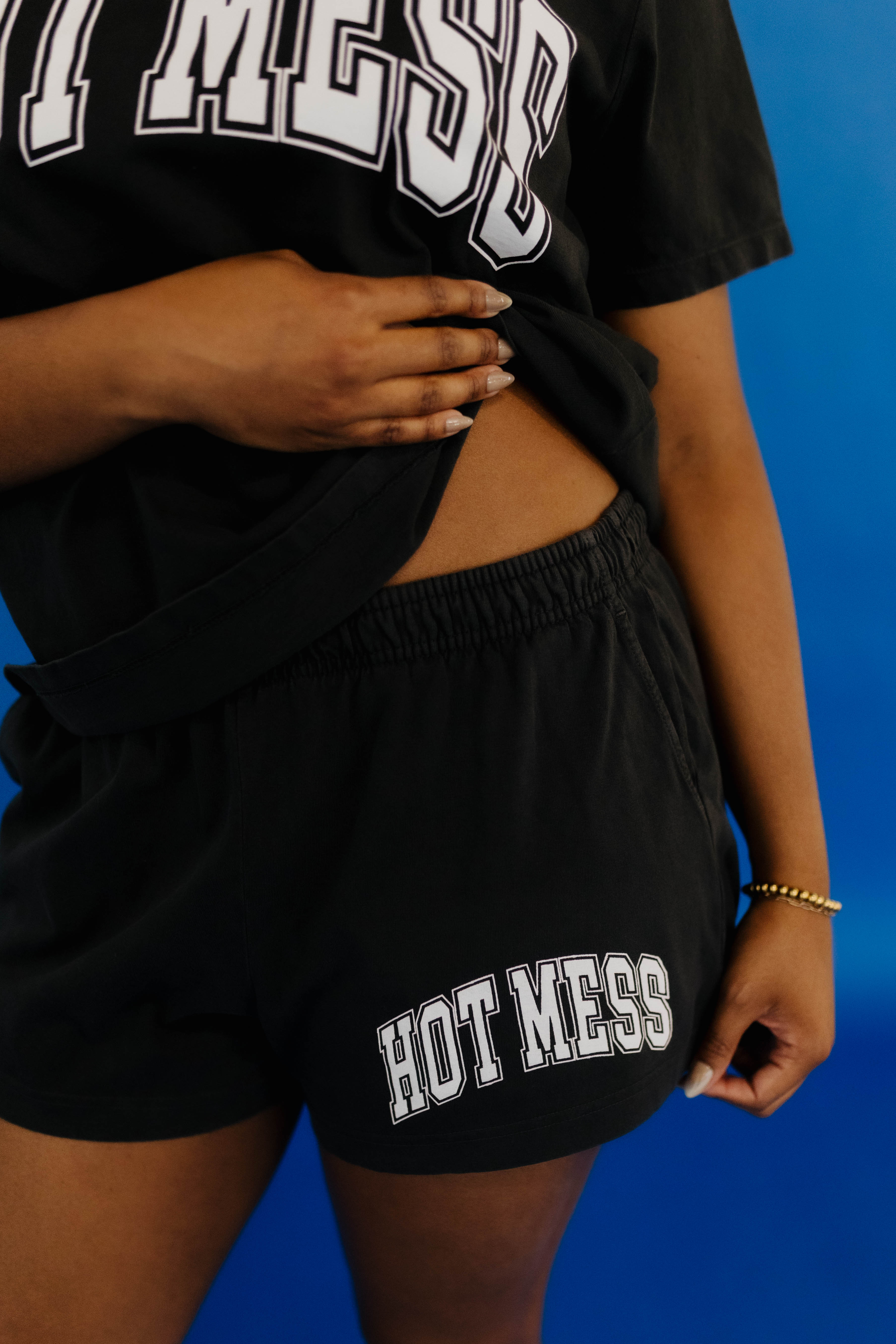 Person wearing a black t-shirt and shorts with 'HOT MESS' text on a blue background
