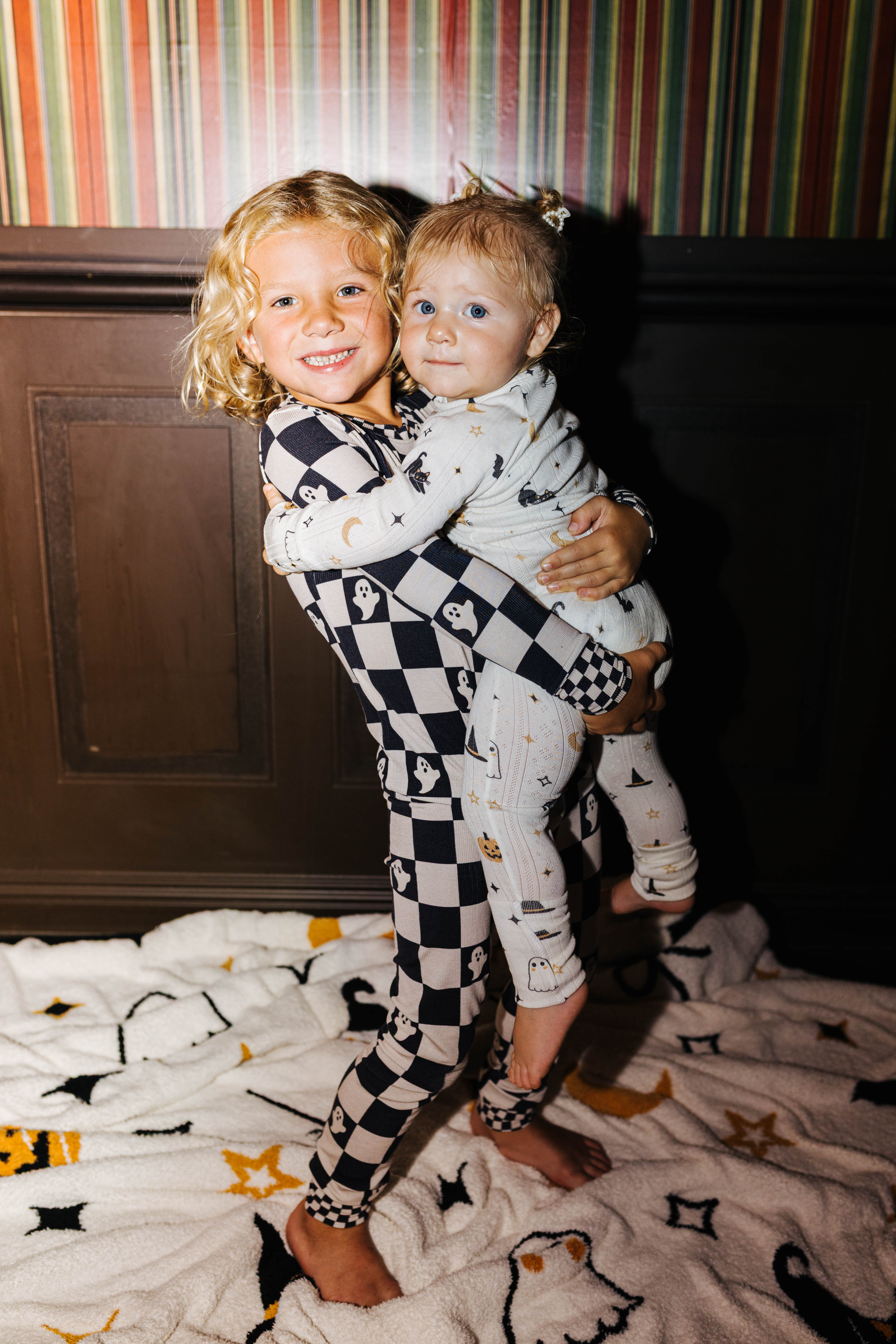 Two young children wearing halloween pjs one holding the other