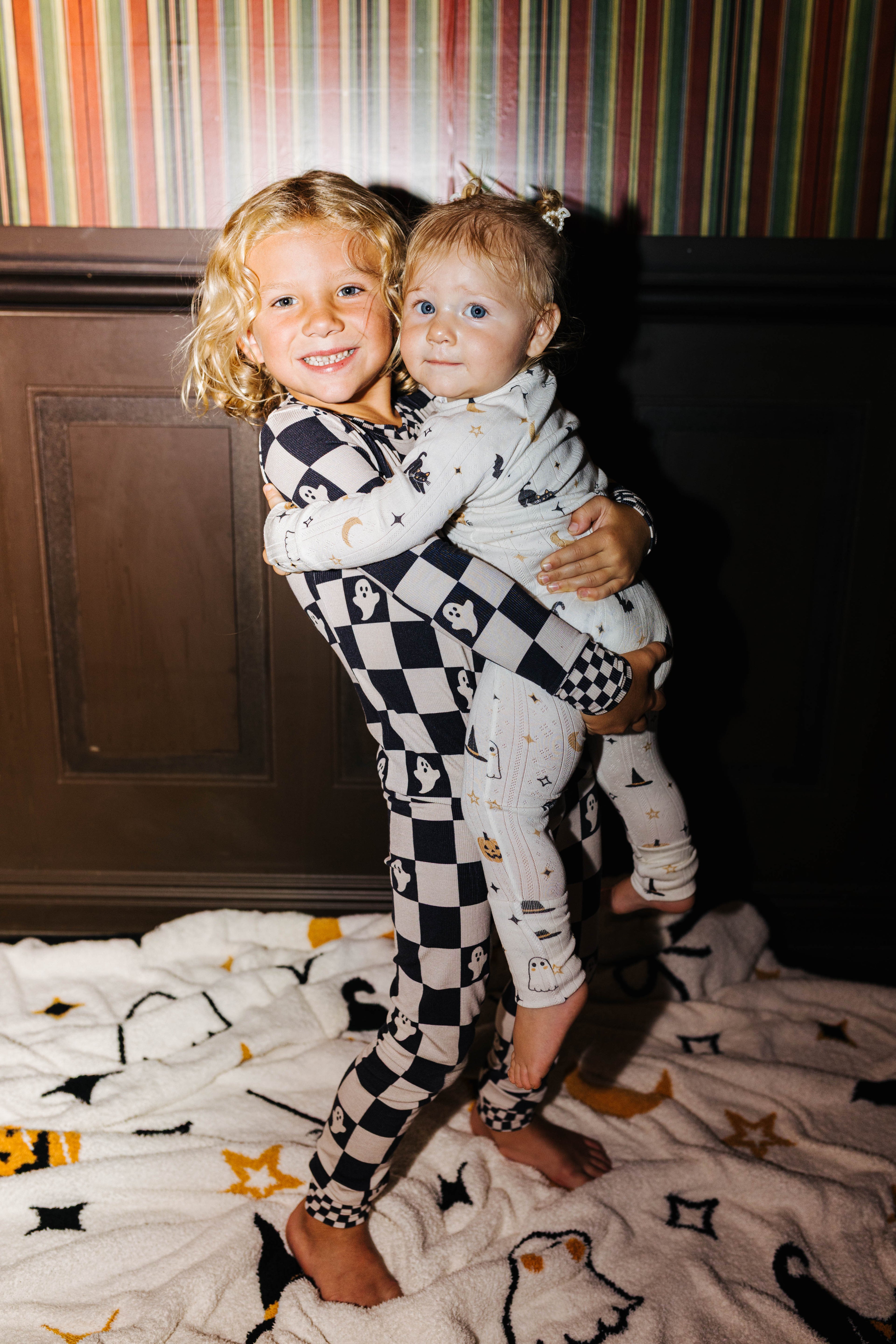 Two young children wearing halloween pjs one holding the other