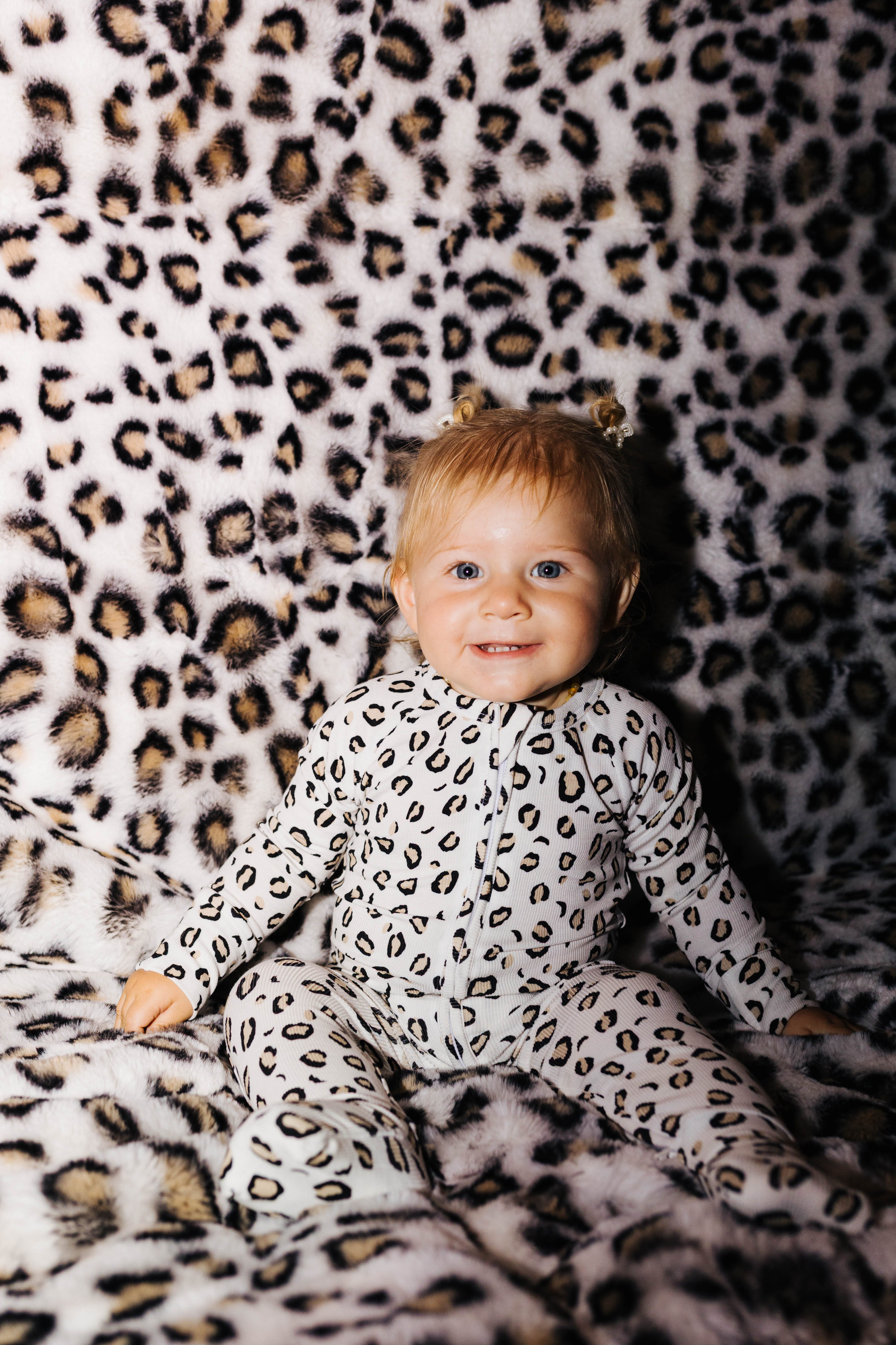 Baby wearing leopard zip pajamas on a leopard blanket
