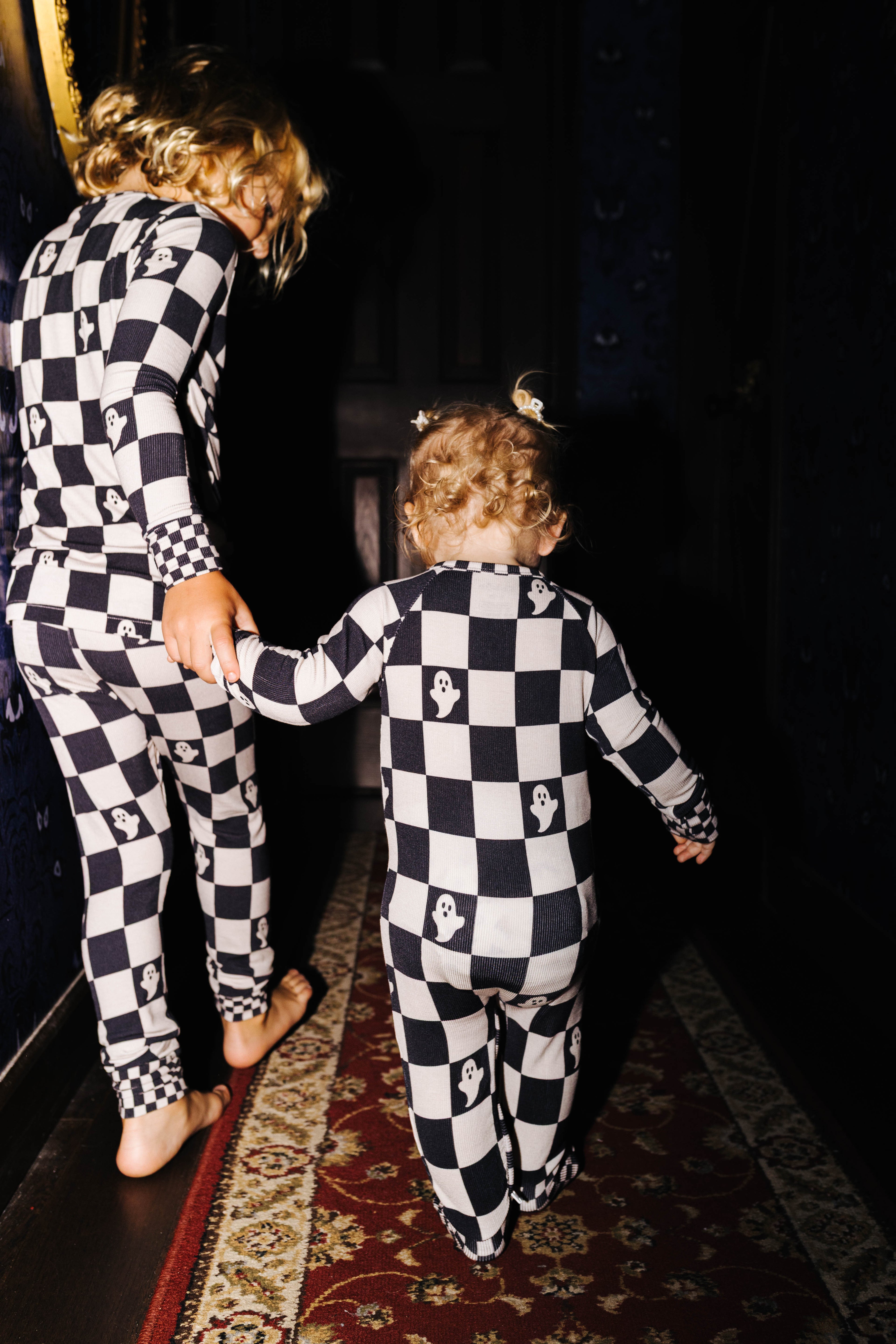 Back view of baby Ghost Check zip pajamas beside an older child