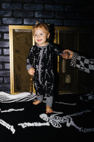 Baby wearing Skelly zip pajamas in front of a fireplace