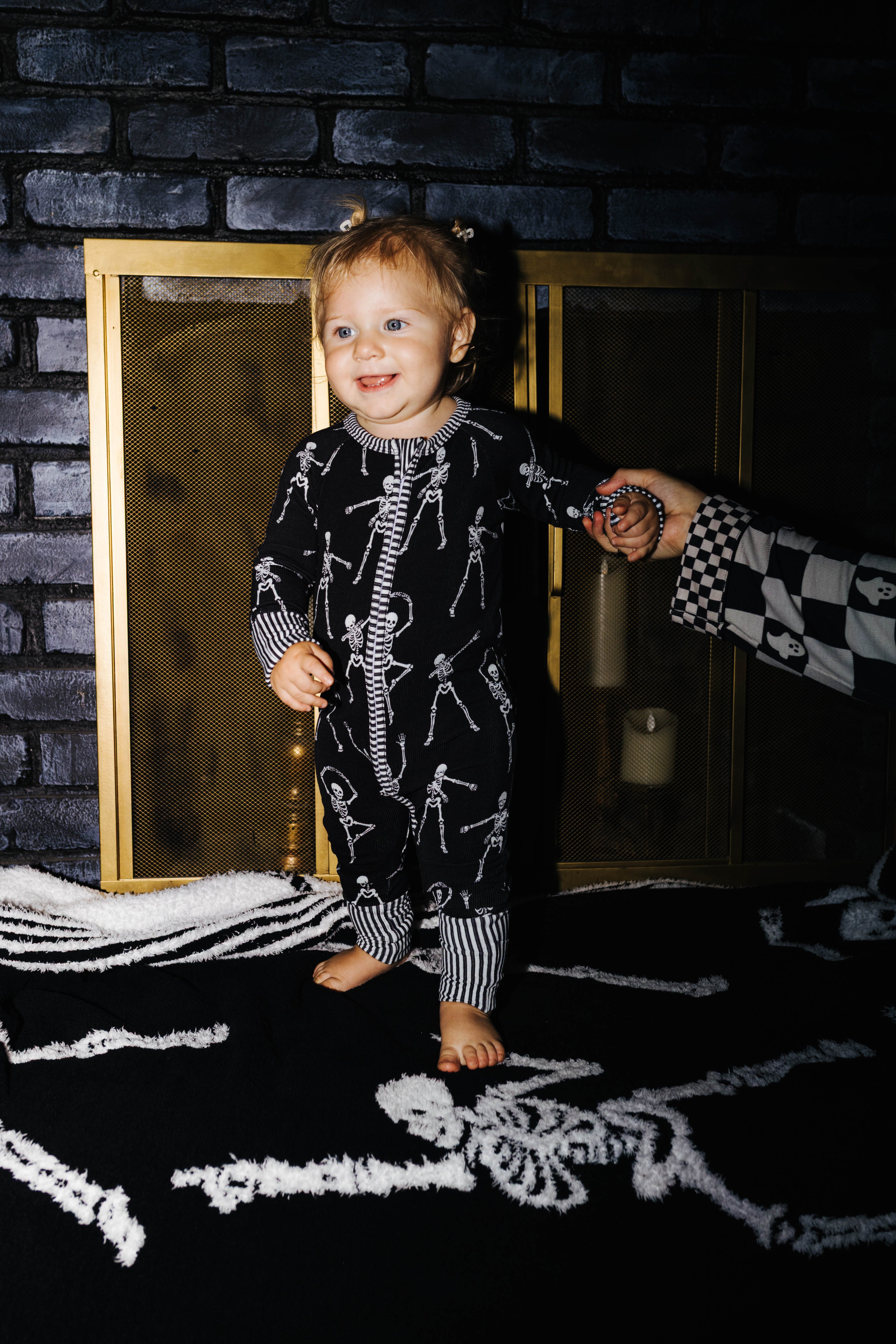 Baby wearing Skelly zip pajamas in front of a fireplace