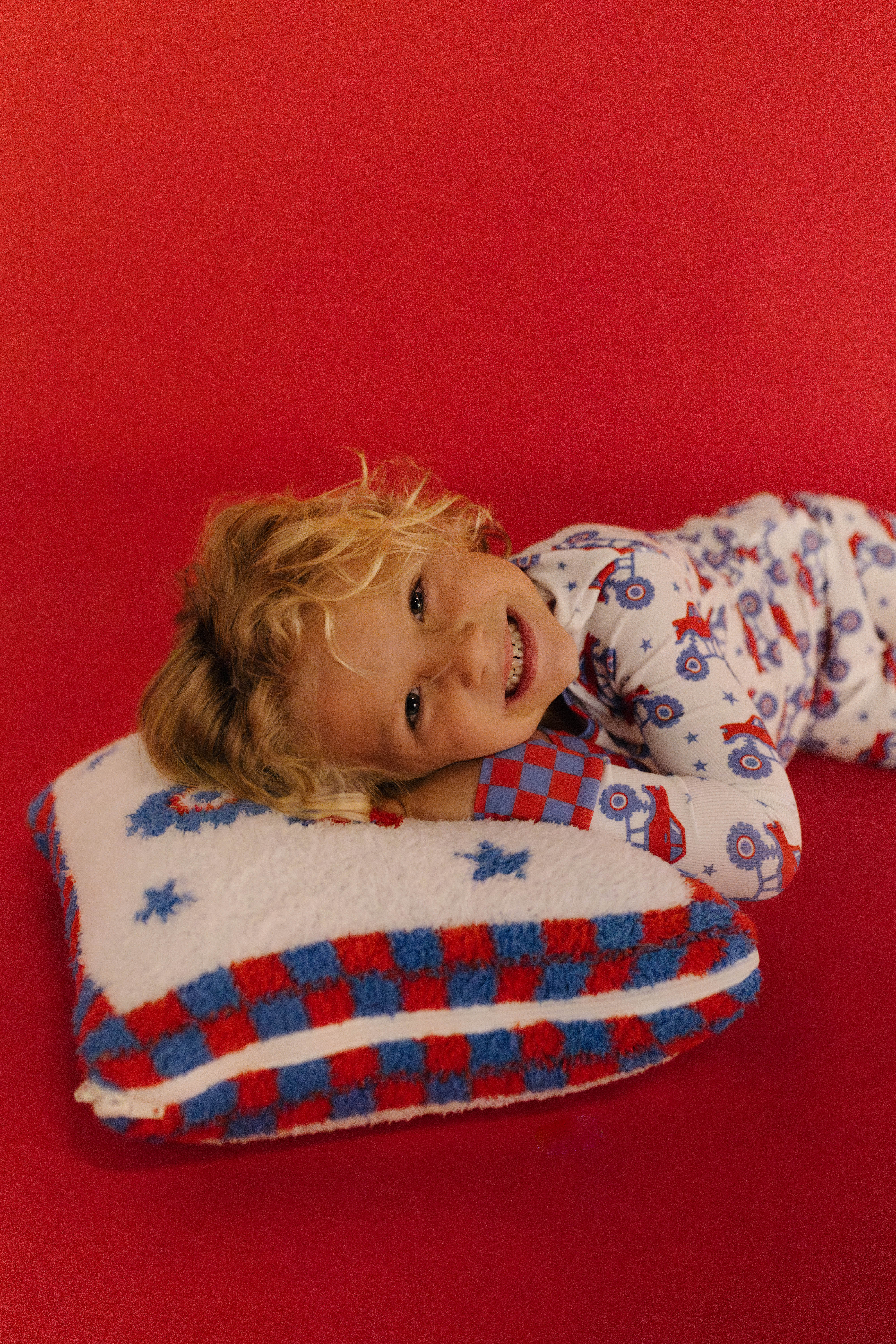 Child in pajamas with a red, white, and blue checkered quillow on a red background