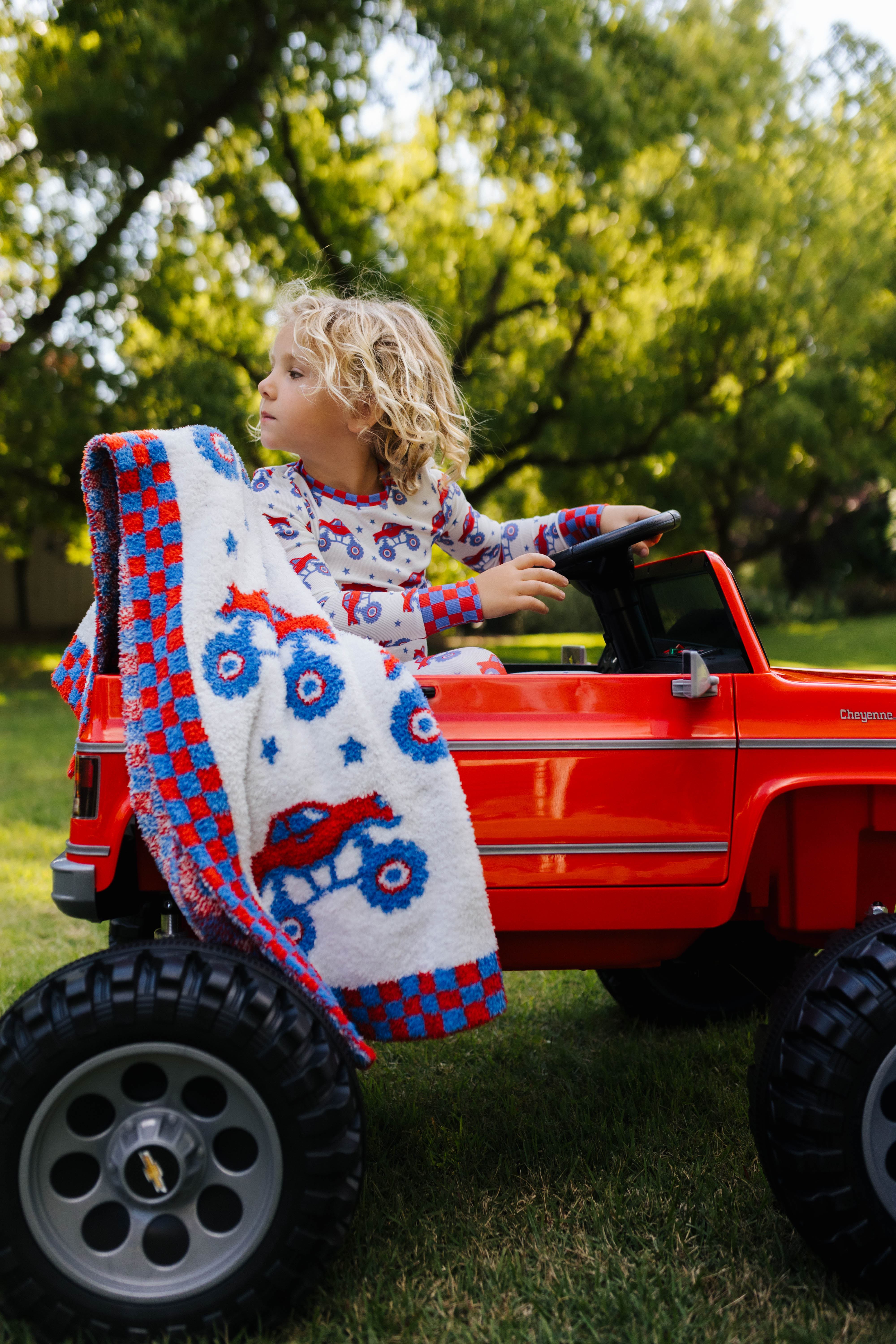 Child playing with a red toy truck outdoors, with the blanket decor