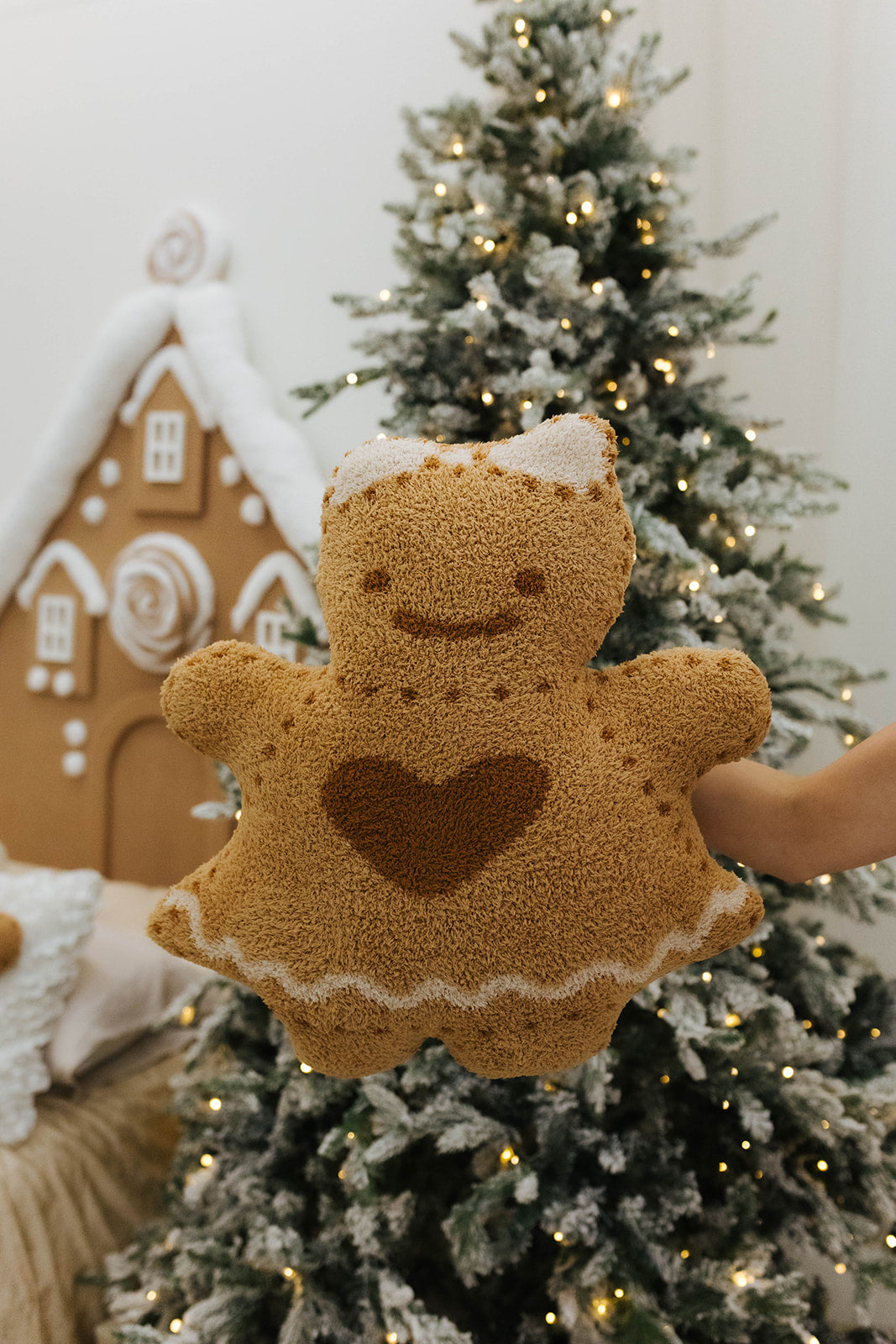 Gingerbread-shaped plush toy held in front of a decorated Christmas tree.