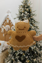Gingerbread-shaped plush toy held in front of a decorated Christmas tree.