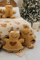 Gingerbread-themed plush toys on a decorative blanket with a Christmas tree in the background.
