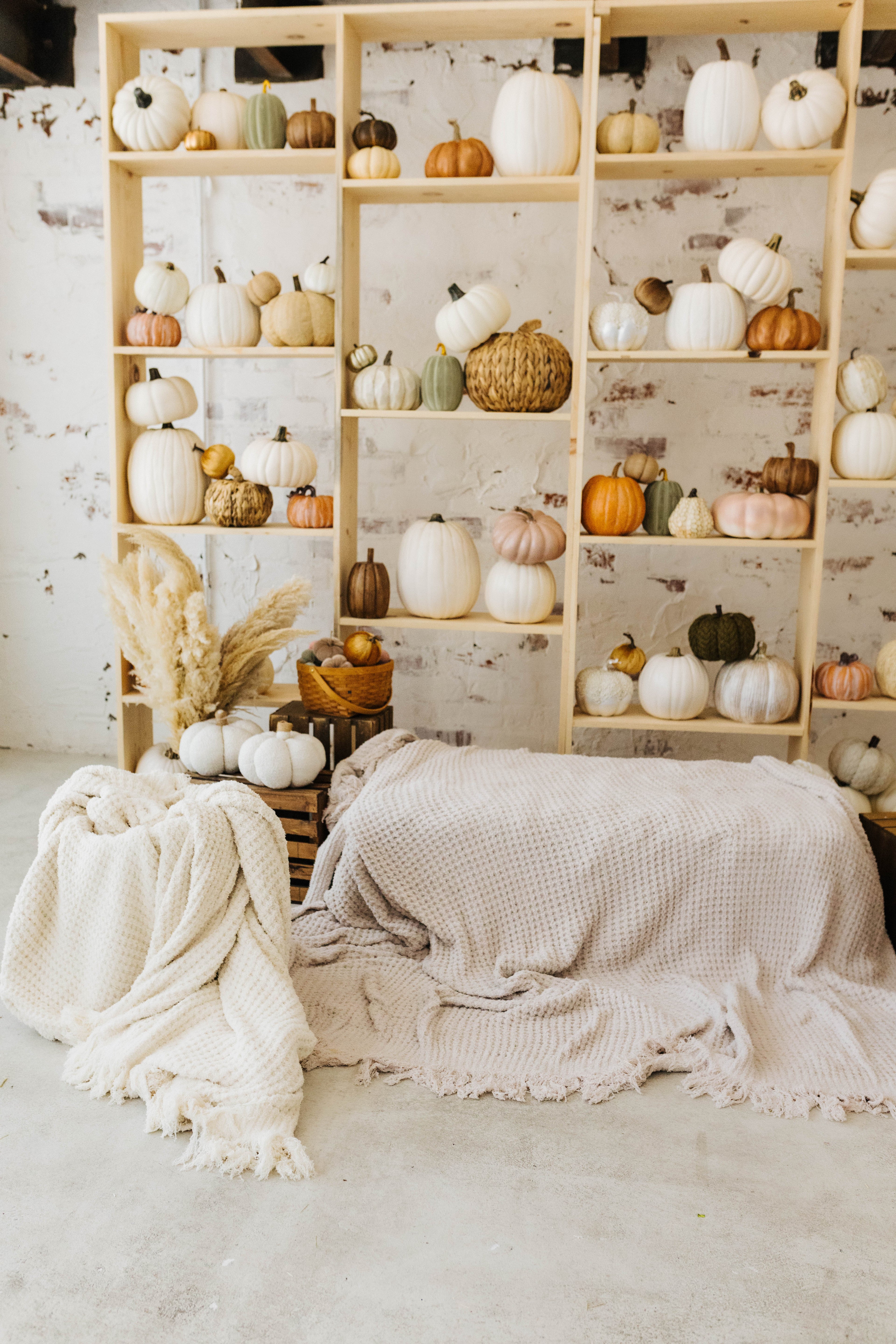 sand waffle blanket sitting in the basket neatly and cream waffle blanket laying on the hay with pumpkin decorations in the background 