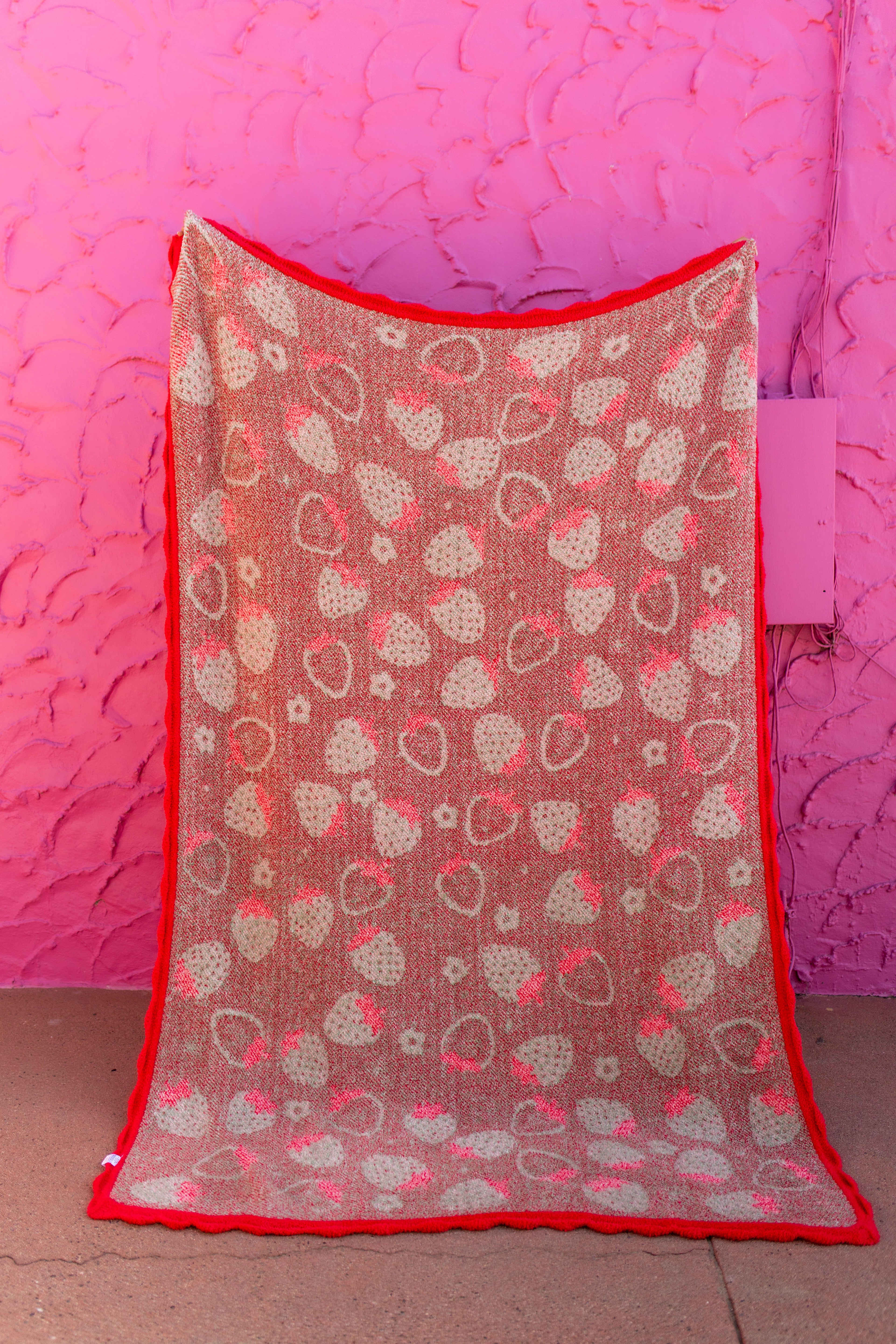 Back of the strawberry blanket showing the mostly red/green print held against a pink background