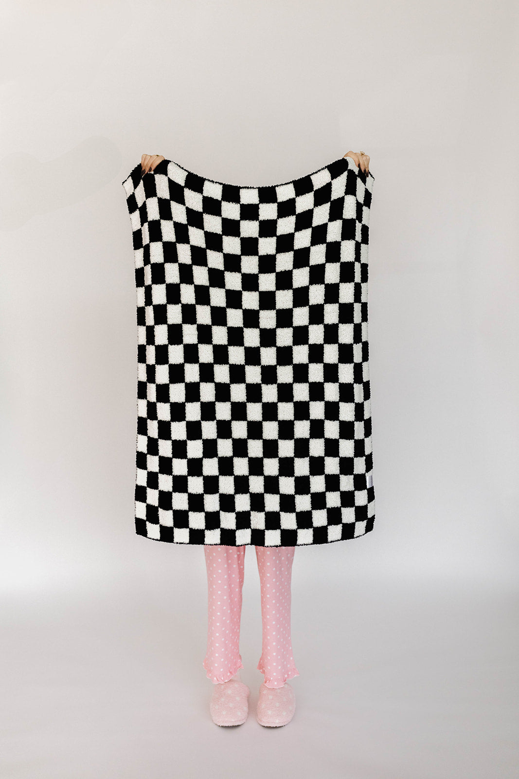 Person holding a black and white checkered blanket on a plain background