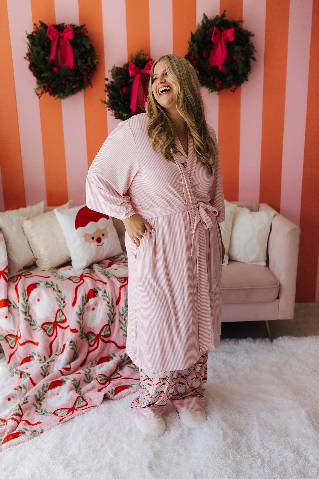 Woman in a pink robe standing in a room with Christmas decorations.