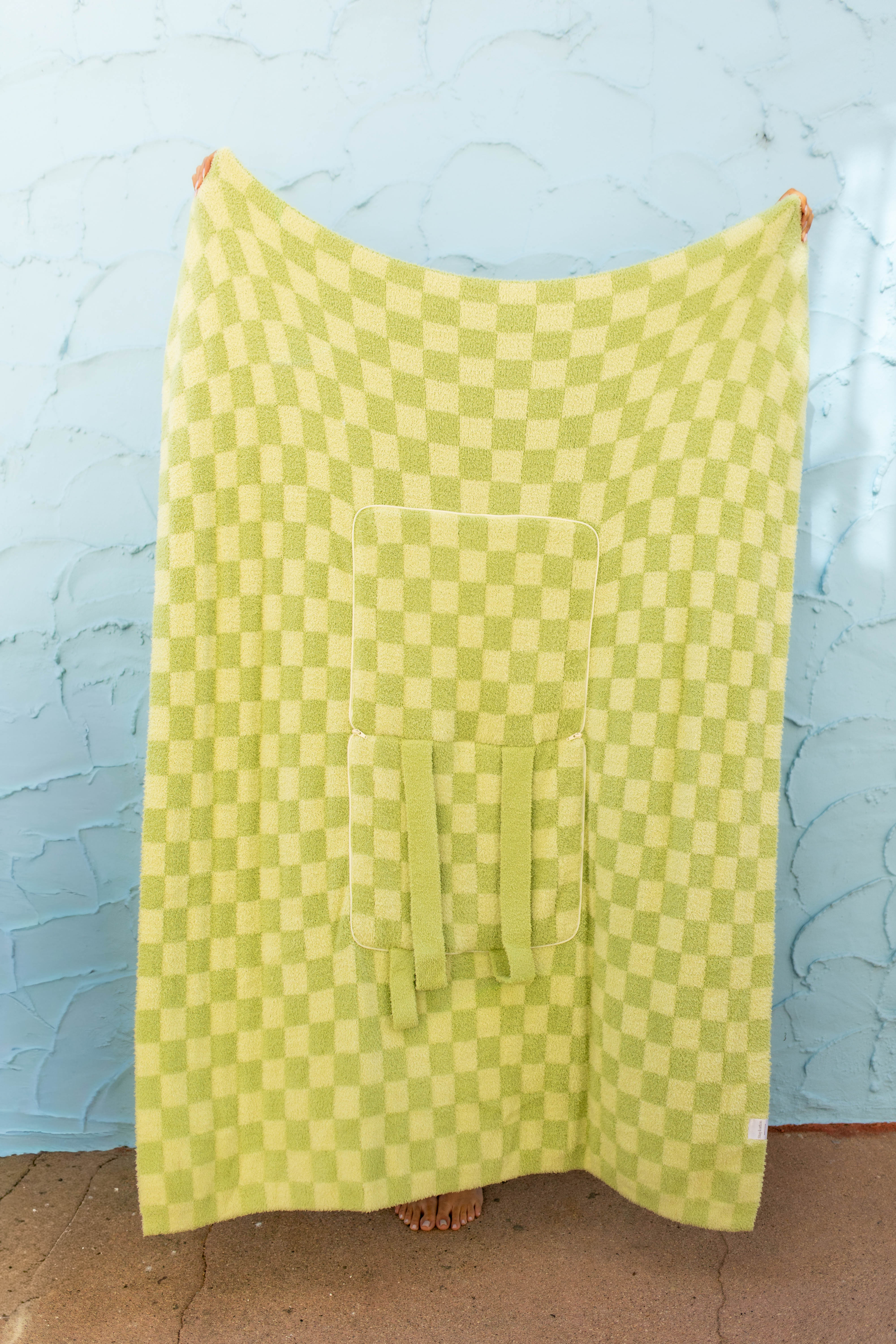 Front of the green check quillow , hanging against a light blue textured wall.