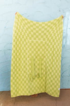 Front of the green check quillow , hanging against a light blue textured wall.