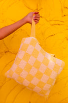 A knit check quillow held by a person's hand against a bright yellow textured background.
