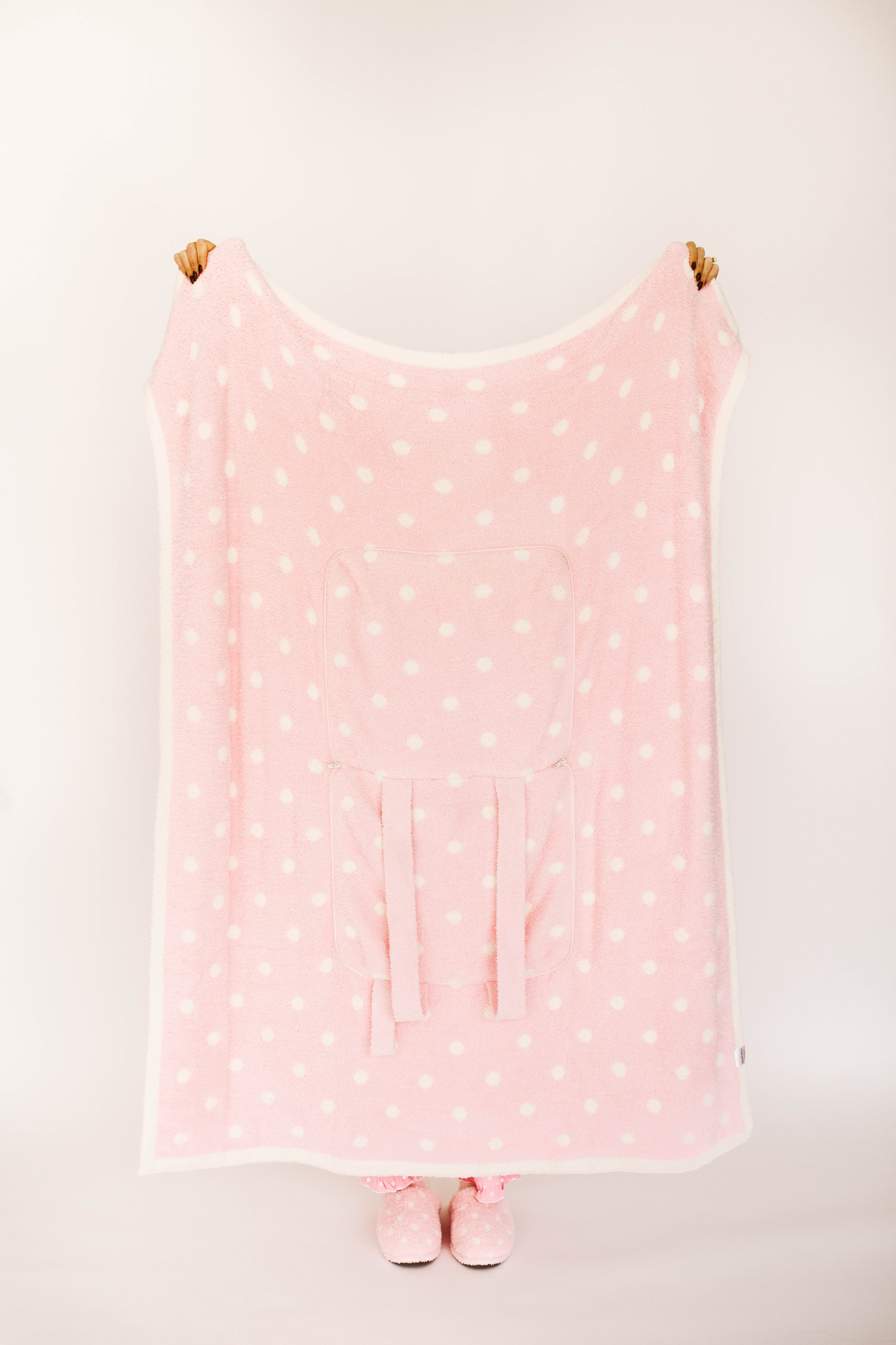 Pink polka dot blanket with matching slippers on a white background