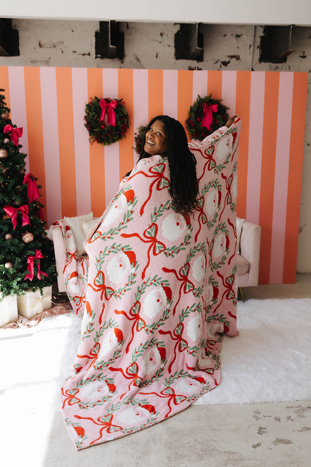 Woman wrapped in a festive blanket with a Christmas tree and striped wall in the background