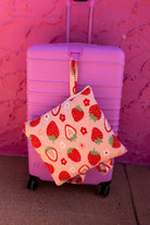 Our outdoor quillow with a strawberry and hanging from a pink suitcase against a pink textured wall.