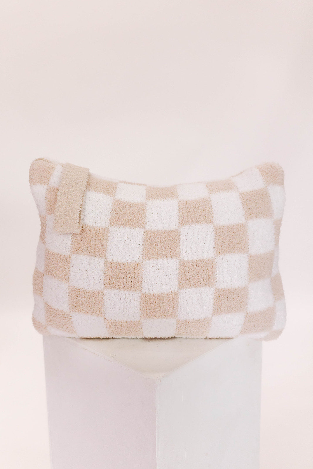 Checkered pillow with beige and white pattern on a light pink background