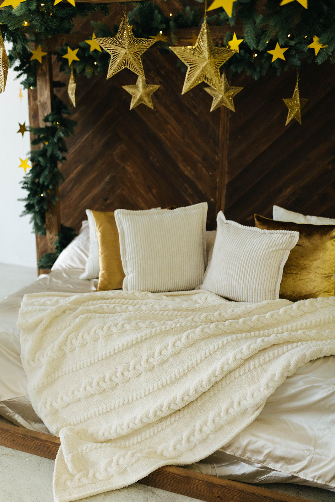Decorative bed with white bedding and gold pillows, surrounded by Christmas decorations including stars and greenery.