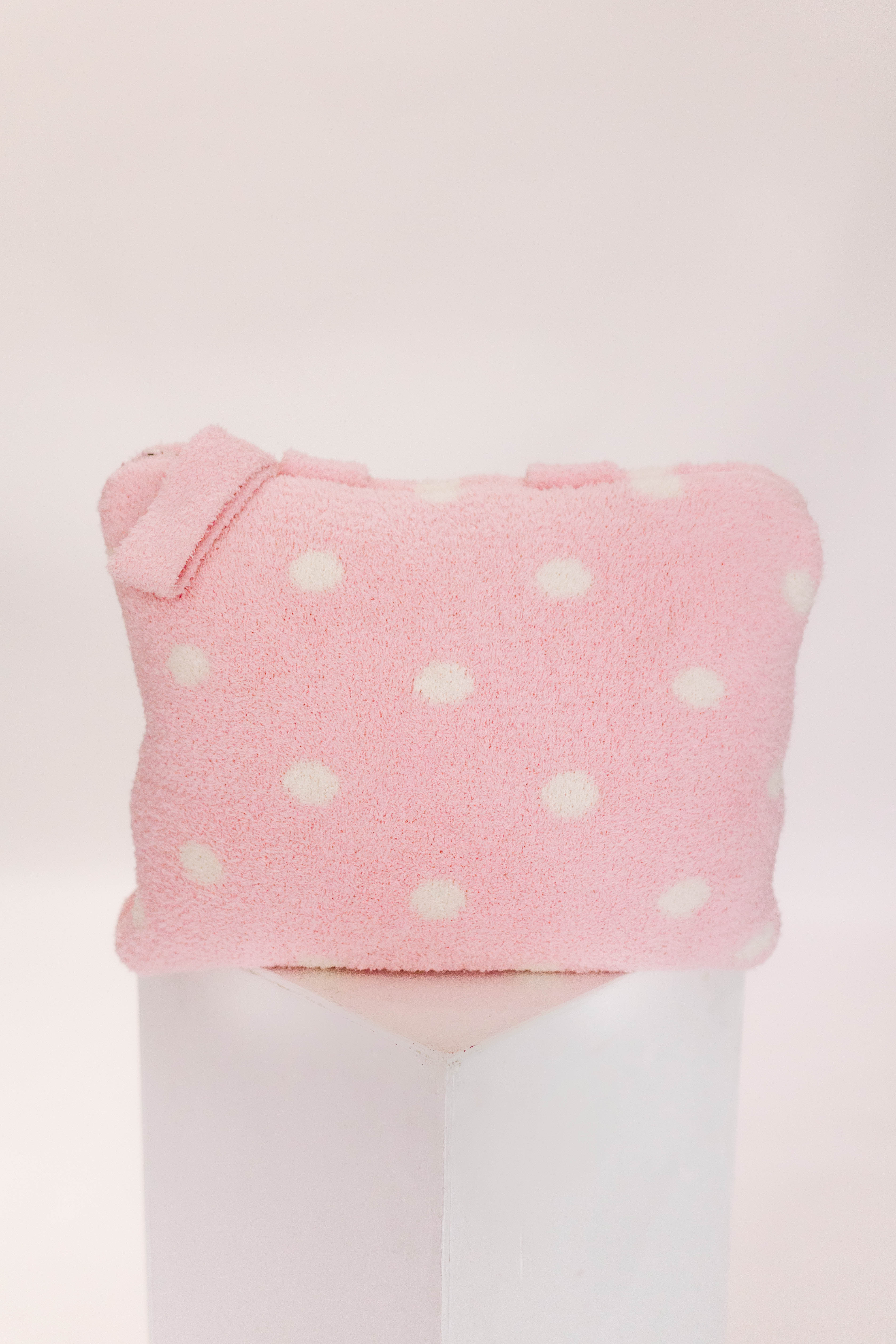 Pink polka dot pillow on a pillar against a white background