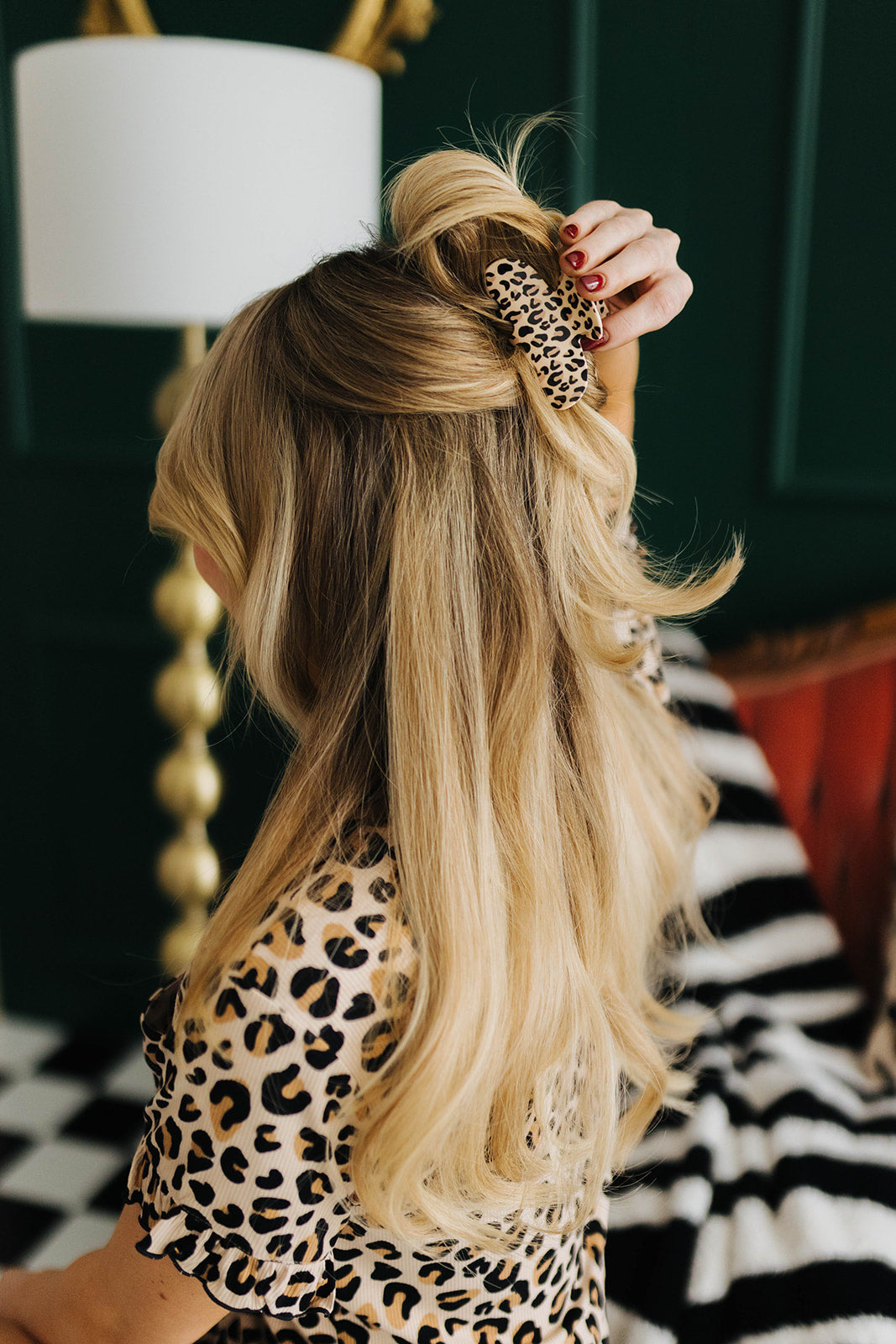 Person with long blonde hair styled in a high ponytail, wearing a leopard print pajama top and claw clip
