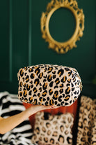 Leopard print cosmetic bag held by a hand against a green wall with a decorative mirror.