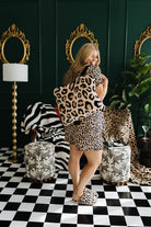Woman in leopard print outfit standing in a stylish room with checkered floor and decorative mirrors.