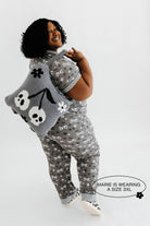 model mari wearing a size 3x in the skeleton pajamas holding the skeleton backpack and wristlet quillow over shoulder 