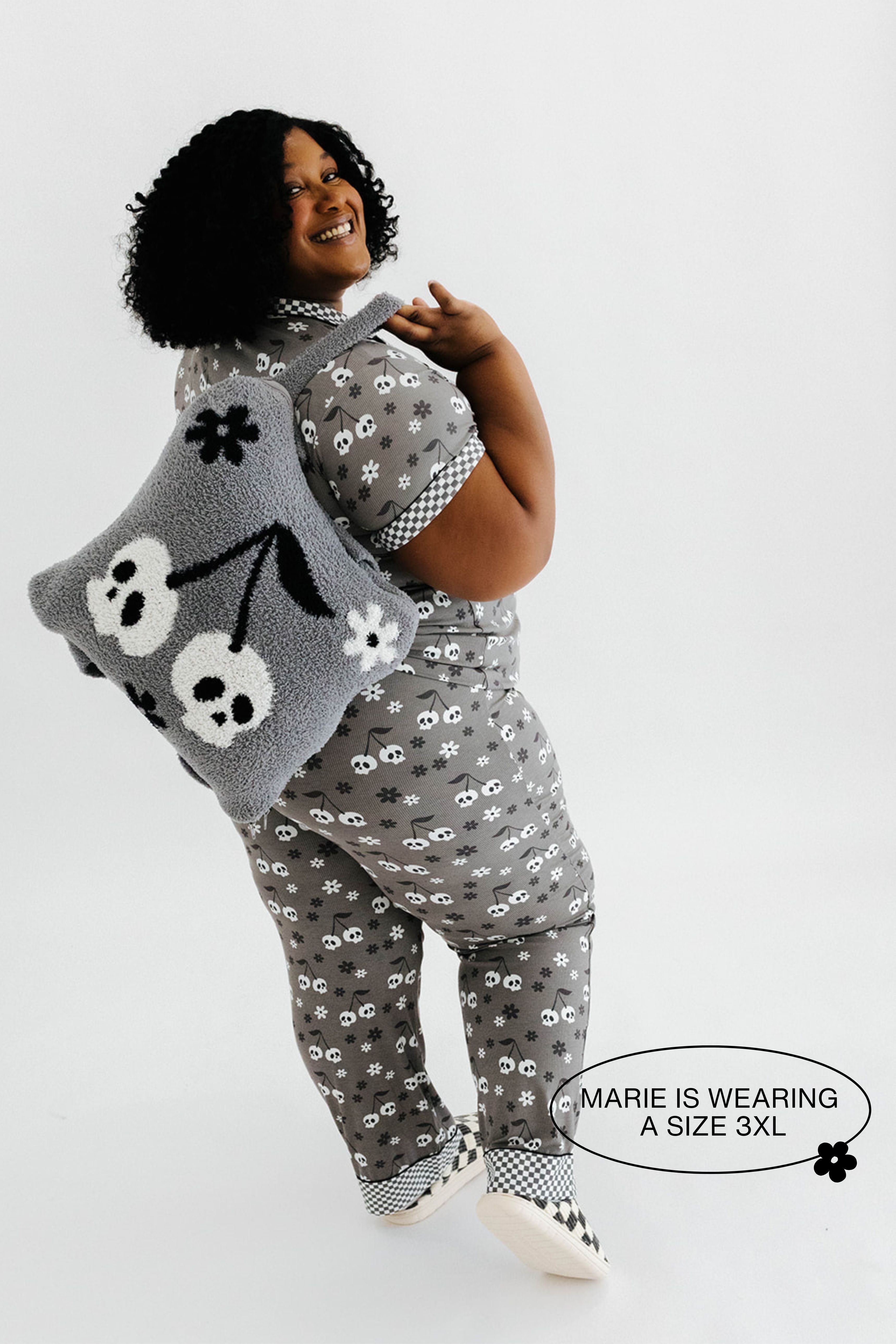 model mari wearing a size 3x in the skeleton pajamas holding the skeleton backpack and wristlet quillow over shoulder 