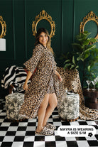 Woman wearing a leopard print robe in a stylish room with mirrors and plants.