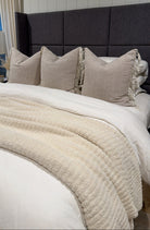 Neatly made bed with beige pillows and blanket against a dark headboard.