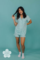 Woman wearing a teal check pajama set against a teal background